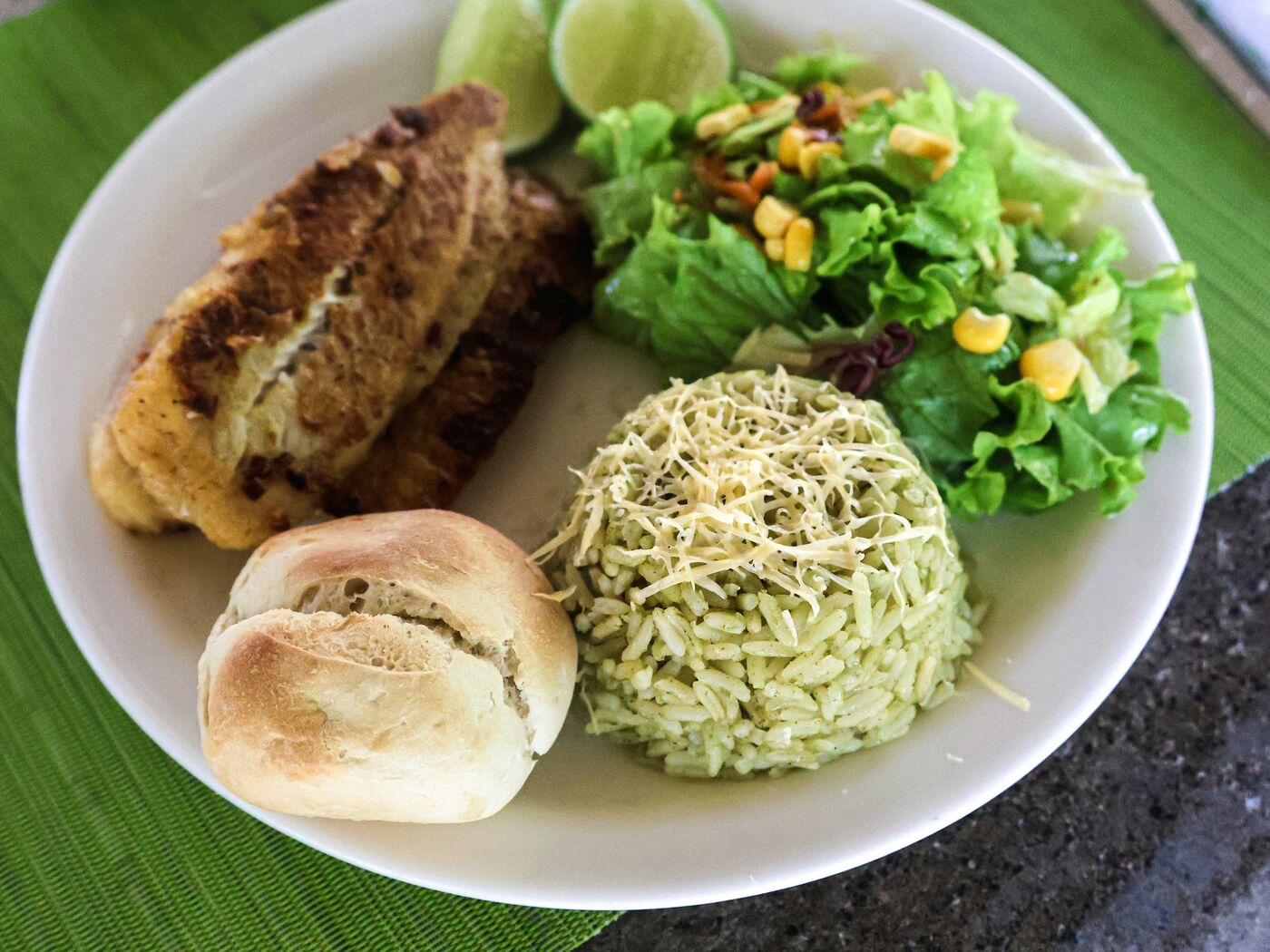 Prato de almoço com filé grelhado, arroz verde com queijo ralado, salada de folhas com milho, pãozinho e limão